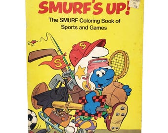 May include: A yellow coloring book titled Smurf's Up! The SMURF Coloring Book of Sports and Games. The cover features a blue Smurf character wearing a red cap and goggles, surrounded by various sports equipment including a bat, ball, and racket.