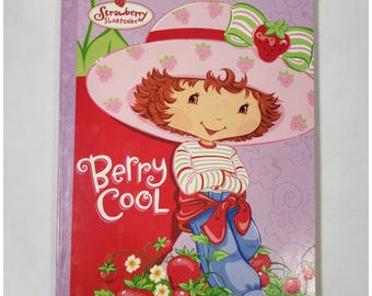 May include: A "Strawberry Shortcake" coloring book with the text "Giant Book to Color With Activities" and "Berry Cool." The cover features a cartoon character wearing a pink hat with strawberries and a red bow. The book has a red and purple cover.