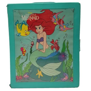 Op de afbeelding: Een turquoise opbergdoos met een kleurrijke illustratie uit Disney's De Kleine Zeemeermin. De afbeelding bevat Ariel, Botje, Sebastiaan en andere personages in een onderwaterwereld. De doos heeft een doorzichtige plastic hoes.