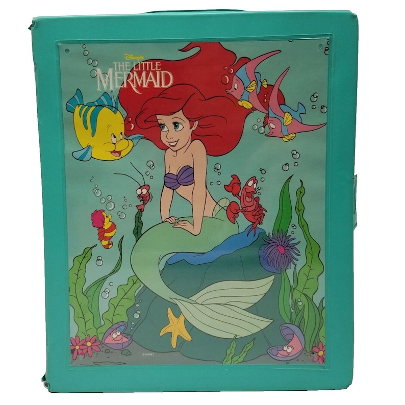 Op de afbeelding: Een turquoise opbergdoos met een kleurrijke illustratie uit Disney's De Kleine Zeemeermin. De afbeelding bevat Ariel, Botje, Sebastiaan en andere personages in een onderwaterwereld. De doos heeft een doorzichtige plastic hoes.