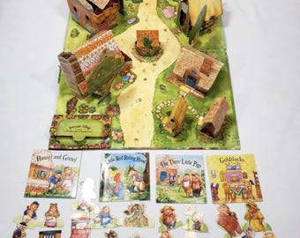 May include: A pop-up book set titled Fairytale Village featuring a three-dimensional landscape with houses, a central path, and various paper character cutouts. Includes four small storybooks: Hansel and Gretel, Little Red Riding Hood, The Three Little Pigs, and Goldilocks and the Three Bears.