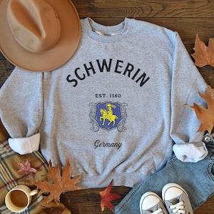 May include: Gray sweatshirt with black text that reads "Schwerin Est. 1160 Germany" and a blue and yellow crest with a knight on a horse.