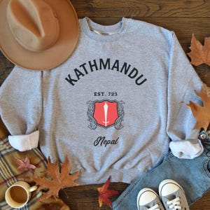 May include: Gray sweatshirt with a black graphic print that says "Kathmandu Est. 723 Nepal" with a red and white shield design.