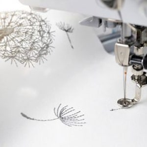 K&ouml;nnte beinhalten: Nahaufnahme einer N&auml;hmaschinennadel, die ein Design von L&ouml;wenzahnblume auf wei&szlig;en Stoff stickt.