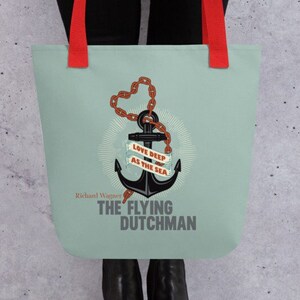 Puede incluir: Una bolsa de tela azul claro con asas rojas presenta un ancla negra con una cadena marrón y una cinta roja que dice "Love Deep As The Sea". El texto "Richard Wagner The Flying Dutchman" está impreso debajo del ancla.