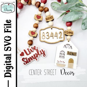 May include: A wooden bead garland with red and white hearts, a house-shaped ornament, and a sign that says "Live Simply". The garland also has a sign with the number "83442" and the word "HOME" on it.