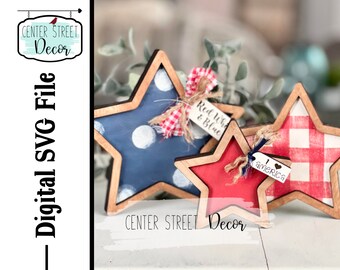Puede incluir: Tres decoraciones de madera en forma de estrella pintadas en rojo, blanco y azul con patrones de cuadros y lunares. Las estrellas tienen un marco de madera y están decoradas con hilo y pequeñas etiquetas que dicen "Red White & Blue" y "I love America".