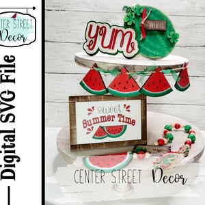 May include: A tiered wooden stand decorated with watermelon themed cutouts. The top tier features a watermelon slice with the word "yum" and a green watermelon cutout with the word "sweet". The middle tier has a watermelon garland and the bottom tier has a sign that says "sweet summer time" with a watermelon slice and a string of red and green beads.