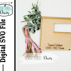 May include: A wooden "E" shaped Tassel Maker with the text "Tassel Maker CENTER STREET Decor". The design includes faux greenery, pink and brown ribbons, and the text "CENTER STREET Decor" and "Digital SVG File".