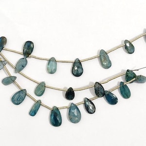 May include: Three strands of blue-green, teardrop-shaped gemstones against a white backdrop. The gemstones, strung on gold-coloured wire, range in shade from light teal to deep indigo. Ideal for jewellery making, these could be components or finished pieces.