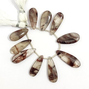 Peut inclure: Un fil de perles en forme de goutte. Les perles sont un mélange de translucide et d'opaque, avec des veines marron et blanches. Les perles sont enfilées sur un fil argenté, et une gland blanc est attaché à l'extrémité.