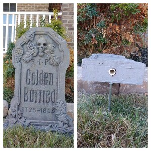 May include: A gray concrete tombstone with the words "R.I.P. Golden Buried 1725-1806" inscribed on it. The tombstone is decorated with a skull and crossbones and floral designs. The tombstone is sitting on a bed of green grass.