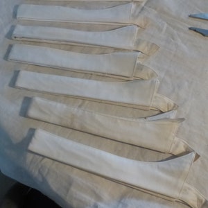 Peut inclure: Une collection de sept cols de chemise blancs, soigneusement disposés sur un tissu clair. Les cols sont pliés et prêts à être cousus, mettant en valeur une esthétique épurée et minimaliste. Les cols sont en tissu doux et clair.