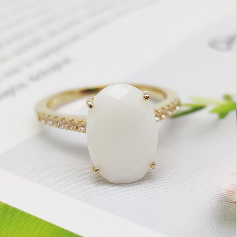 May include: A gold ring with a large white oval gemstone and a band of small clear stones.