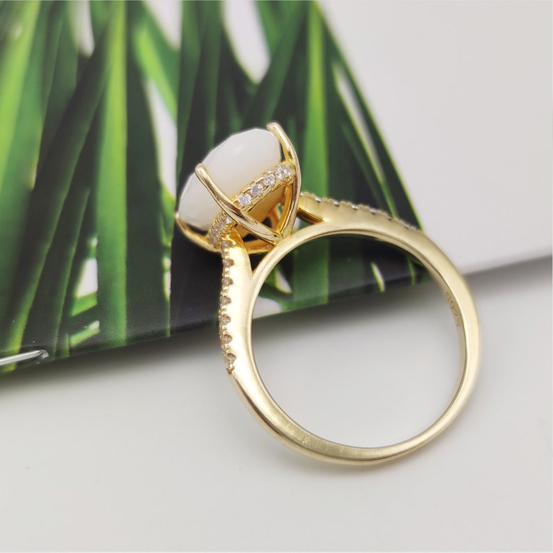 May include: A gold ring with a white oval gemstone and a row of small clear gemstones around the band.