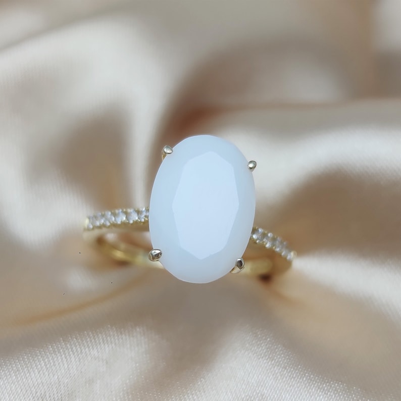 May include: A gold ring with a large oval white gemstone and a band of small clear gemstones.