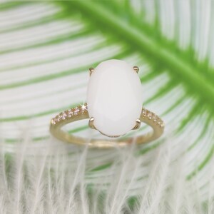 May include: A gold ring with a large oval white gemstone and a band of small clear gemstones.