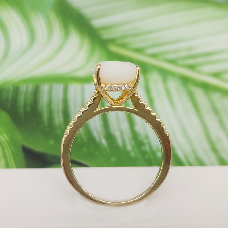 May include: A gold ring with a white oval gemstone and small clear stones around the setting.