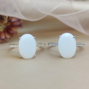 May include: Two oval-shaped rings with white stones set in gold and silver settings. The rings have a row of small clear stones around the band.