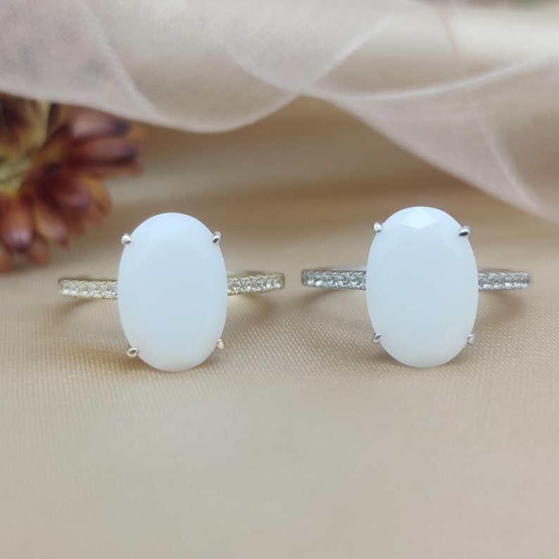 May include: Two oval-shaped rings with white stones set in gold and silver settings. The rings have a row of small clear stones around the band.