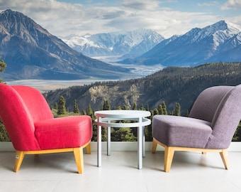 May include: Two chairs, one red and one gray, face each other in front of a white coffee table. The chairs are in front of a wall mural depicting a mountain range with snow-capped peaks and a valley with trees.