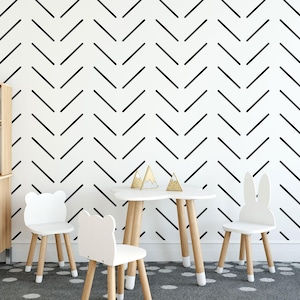 May include: A white play table with four white chairs, two with bunny ears and two with rounded backs. The table and chairs are made of wood and have a natural finish. The background is a white wall with a black chevron pattern.