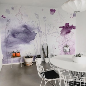 Può includere: Una sala da pranzo moderna con un tavolo bianco e sedie in filo metallico con cuscini neri. La parete presenta un murale floreale con accenti e contorni acquerellati viola. Piante in vaso sono collocate nella stanza.
