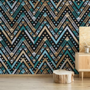 Puede incluir: Una pared cubierta con un patrón de chevron negro, turquesa, beige y blanco. El diseño presenta formas geométricas y líneas punteadas. Un mueble de madera con una planta y velas está a la derecha, y un tocón de madera está en primer plano.