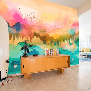May include: A room featuring a colorful abstract mural in shades of pink, yellow, and teal. A wooden cabinet with a black fan and a surfboard are in the foreground. The room has a modern, artistic vibe.