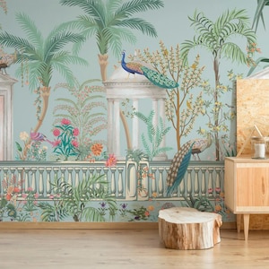 Op de afbeelding: Een muurschildering met een serene tuinscène met palmbomen, klassieke architectuur en pauwen. Het kleurenpalet omvat zachte blauwen, groenen en roze tinten, waardoor een rustige sfeer ontstaat. Het ontwerp omvat een houten kast en een boomstronk.