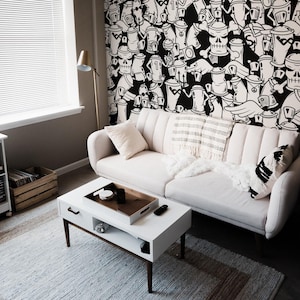Op de afbeelding: Een witte bank met zwart-witte kussens staat in een woonkamer met een witte salontafel en een witte platenspelerstandaard. De muur achter de bank is bedekt met een zwart-witte graffitimuurschildering van spuitbussen.