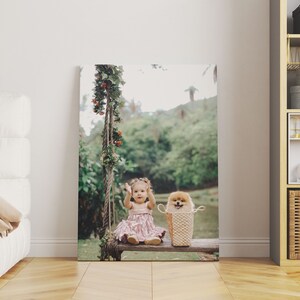 May include: A canvas print featuring a young child in a pink dress and a small dog in a woven basket, seated on a wooden swing. The swing is adorned with greenery and red berries, set against a blurred outdoor backdrop.