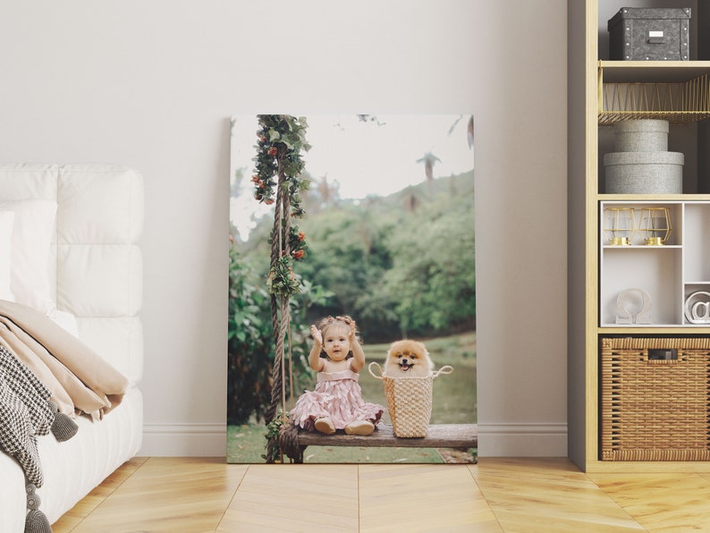 May include: A canvas print featuring a young child in a pink dress and a small dog in a woven basket, seated on a wooden swing. The swing is adorned with greenery and red berries, set against a blurred outdoor backdrop.