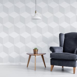 May include: A modern living room scene featuring a dark gray armchair, a small wooden side table with a potted plant, and a geometric cube-patterned wall. A white pendant light hangs above the table, creating a minimalist aesthetic.