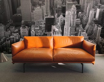 May include: A brown leather sofa with a black metal frame sits in front of a black and white cityscape mural.