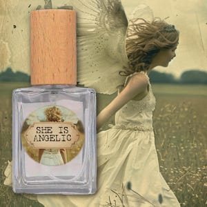 Puede incluir: Un frasco de perfume rectangular transparente con una tapa de madera clara. La etiqueta dice "SHE IS ANGELIC" sobre una imagen de una mujer con un vestido blanco. El fondo presenta a una mujer con alas de ángel en un campo.