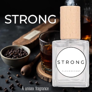 May include: A clear, square perfume bottle with a light wood cap. The label reads "STRONG" in a black circle, with "CLOUD9SCENT" below. The image includes a glass of amber liquid, a bowl of peppercorns, and the text "A unisex fragrance".