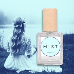 May include: A clear glass perfume bottle with a light wood cap and a white label with the word "MIST" in black. The background features a woman in a white dress and a floral crown, sitting near a body of water.