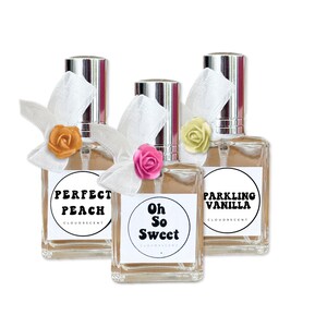 May include: Three perfume bottles with silver caps and white labels. Each bottle has a white bow and a small, colorful rose. The labels read "Perfect Peach", "Oh So Sweet", and "Sparkling Vanilla".