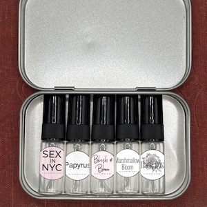 Può includere: Una scatola di metallo argentato contenente cinque piccoli flaconi spray in vetro trasparente con tappi neri. Ogni flacone presenta un'etichetta circolare con il testo: Sex in NYC, Papyrus, Blush & Bloom, Marshmallow Bloom e Black Rose, marchio Cloudscent.