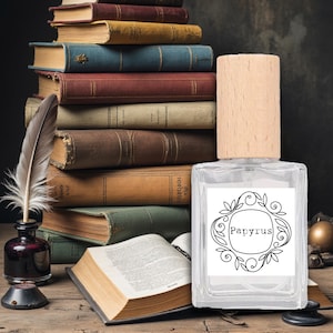 Puede incluir: Un frasco de perfume de vidrio transparente con una tapa de madera y una etiqueta blanca que dice "Papyrus" en un marco decorativo. Una pila de libros antiguos y una pluma en un tintero en el fondo.
