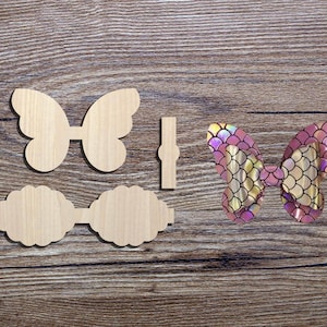 Puede incluir: Piezas de artesanía de madera en forma de mariposa y un lazo terminado con escamas de sirena. Las piezas sin terminar son de color marrón claro, mientras que el lazo presenta escamas iridiscentes rosas, doradas y moradas. Ideal para manualidades.