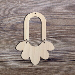 Peut inclure: Composants de boucles d'oreilles en bois non finis. L'ensemble comprend une pièce supérieure arquée et une pièce inférieure en forme de fleur, chacune avec des trous pré-percés pour l'assemblage. Le grain naturel du bois est visible sur un fond en bois brun.