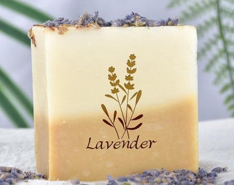 May include: A rectangular bar of soap with a light brown and white color gradient. The soap has a lavender scent and is decorated with a gold silhouette of lavender flowers and the word "Lavender".