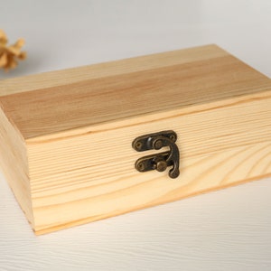 May include: A natural wood box with a hinged lid and a brass latch. The box is made of light wood with a natural finish.