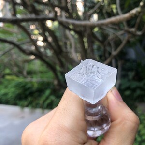 May include: A clear plastic stamp with the word "nice" embossed on the top. The stamp is attached to a clear plastic handle.