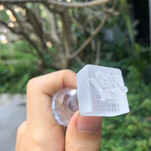 May include: A clear plastic stamp with a raised design. The stamp is held in a hand.