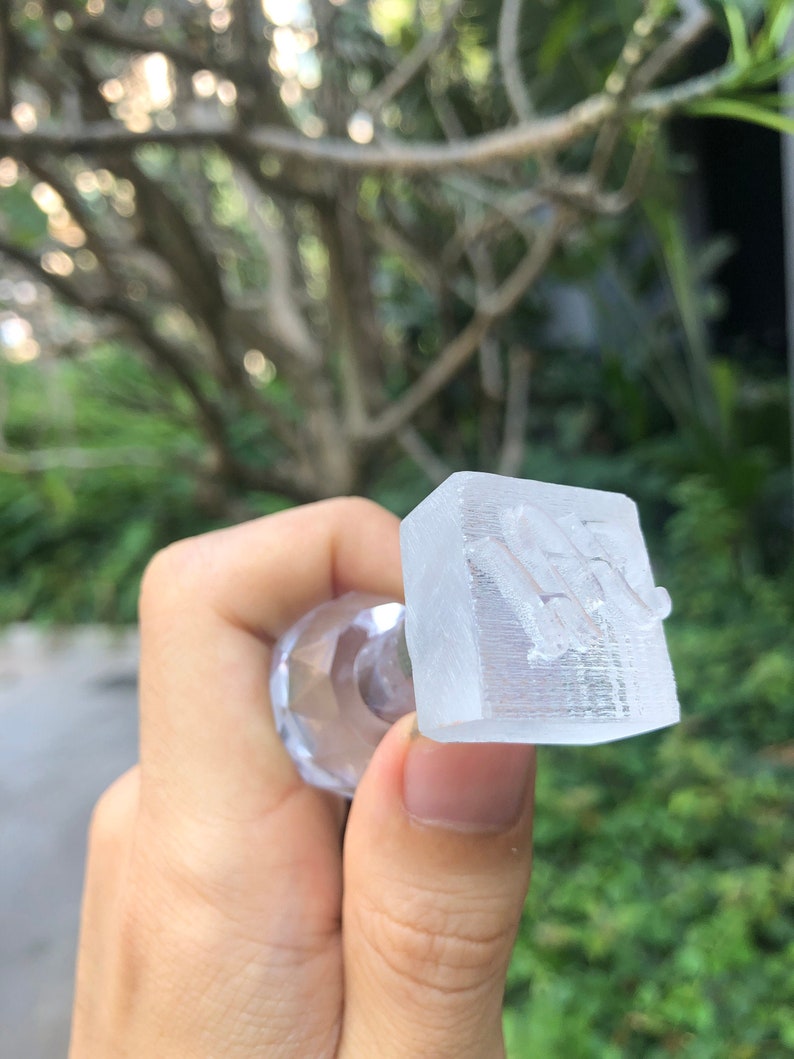 May include: A clear plastic stamp with a raised design. The stamp is held in a hand.