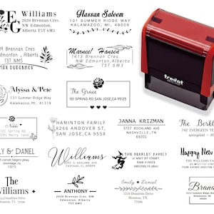 May include: A red and black Trodat self-inking stamp next to various custom address stamps. The stamps feature names, addresses, and decorative elements like flowers and leaves. Ideal for personalized stationery.