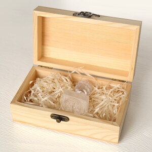 May include: A wooden box with a hinged lid, open to reveal a clear glass stamp inside. The box is filled with shredded paper for cushioning.